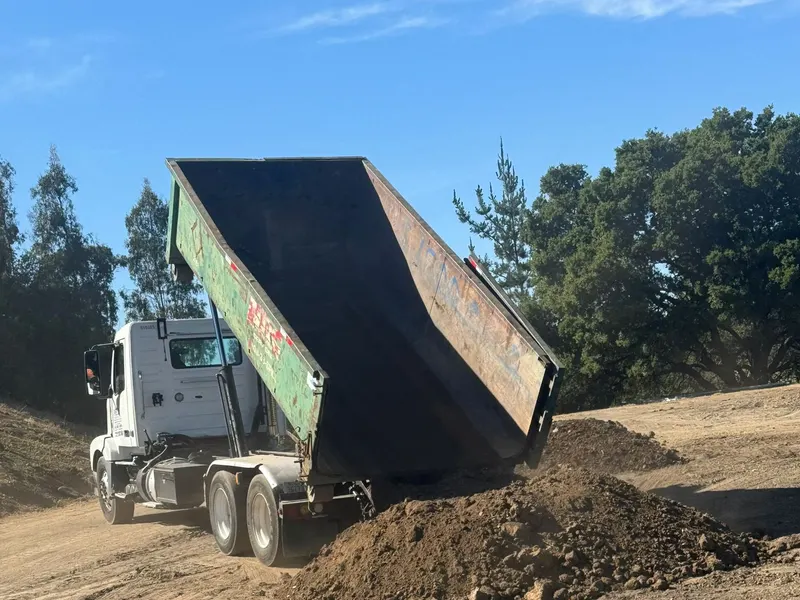 Dump truck with a raised bed unloading fill dirt onto an open site