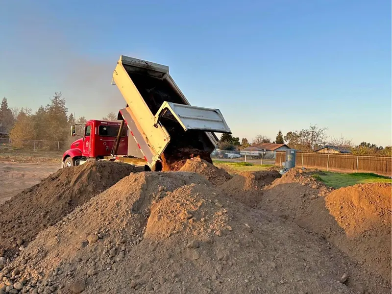 Red dump truck unloading a load of fill dirt at a project site